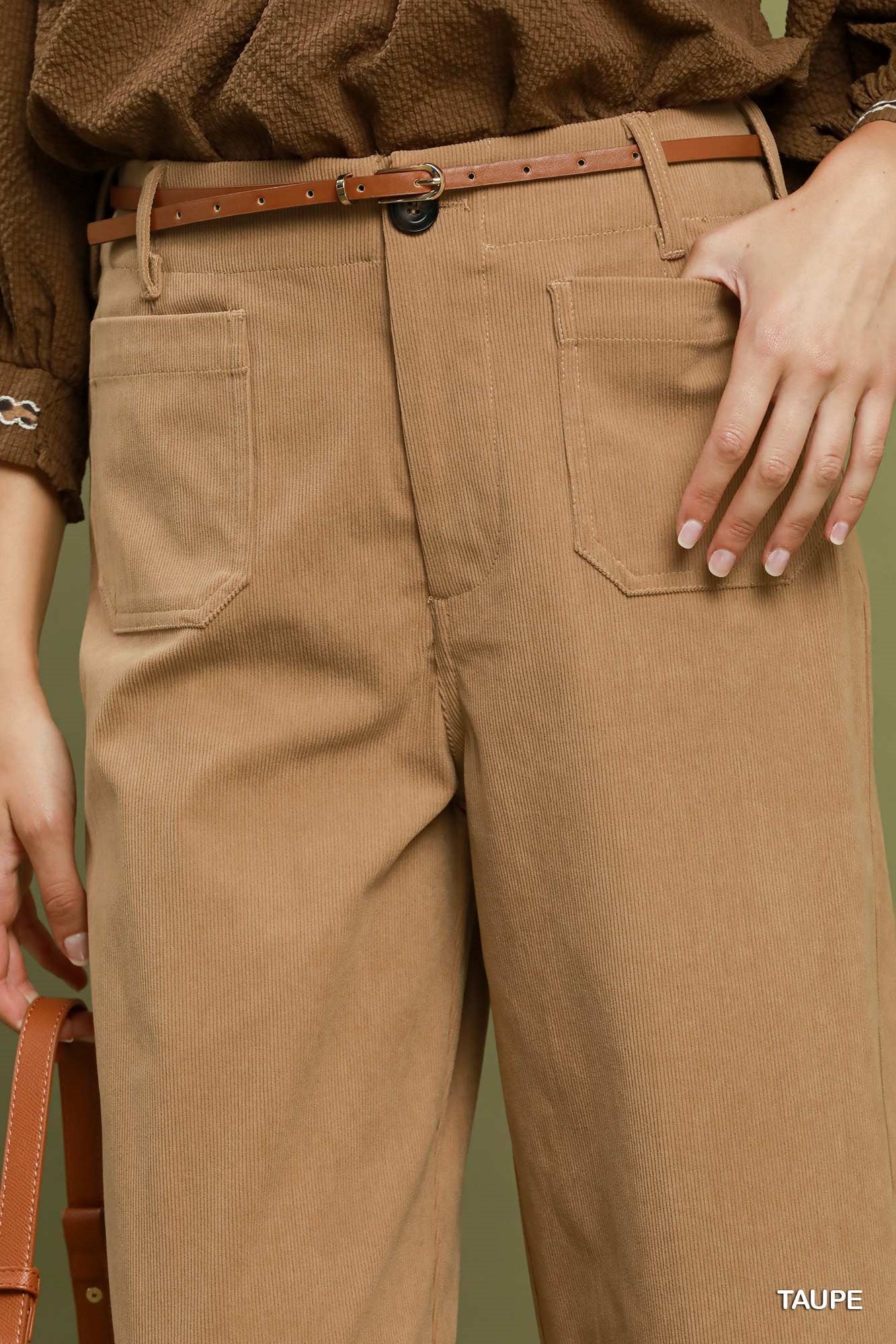A close-up of a person wearing taupe wide-leg trousers with a brown belt, a brown textured top, and a hand resting on the pocket. The color 'TAUPE' is printed in the bottom right corner.