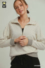Woman wearing a cream and black polka dot jacket on a plain background