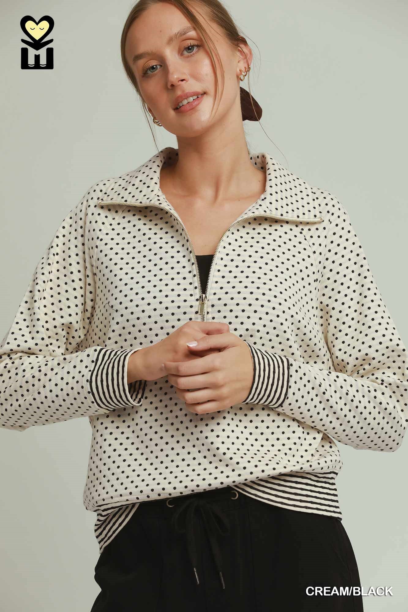 Woman wearing a cream and black polka dot jacket on a plain background