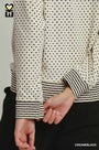 Close-up of a cream-colored long-sleeve top with black polka dots and black-and-white striped cuffs and hem, worn by a model.