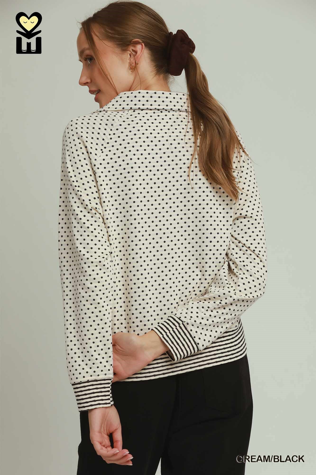 Woman wearing a cream blouse with black polka dot pattern and striped sleeves on a plain background
