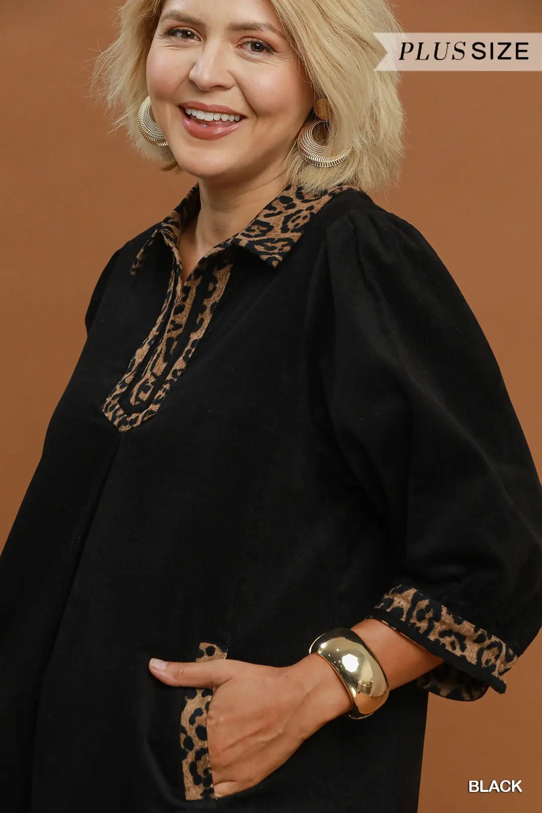 A woman wearing a black blouse with leopard print trim on the collar and cuffs, posed against a solid brown background. A 'PLUS SIZE' label is visible in the top right corner, and 'BLACK' is labeled in the bottom right corner.