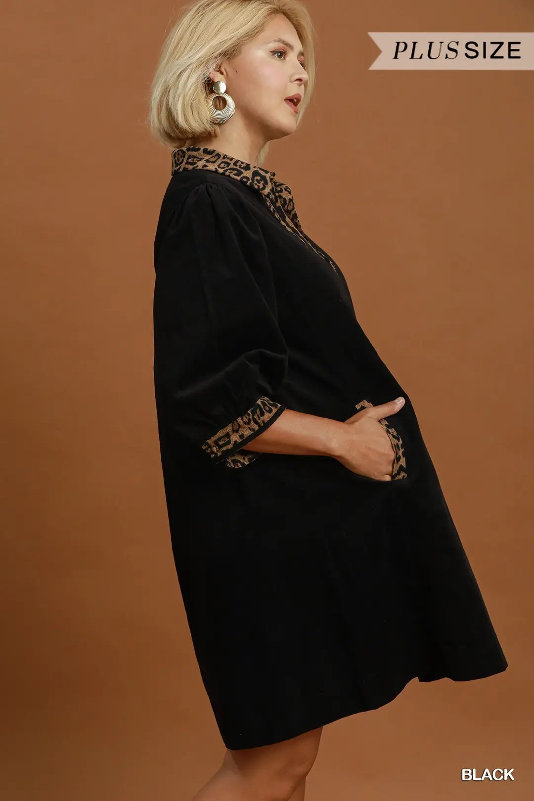 A woman modeling a black plus-size dress with leopard-print trim at the collar and cuffs, posed against a solid warm brown studio background. Text overlays read 'PLUS SIZE' and 'BLACK'.