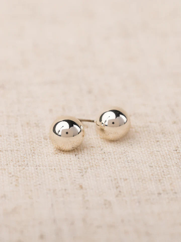 Pair of silver round earrings on a beige fabric background