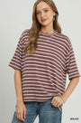 A woman wearing an oversized short-sleeve t-shirt with horizontal mauve and white stripes, paired with blue jeans, against a light gray studio background.