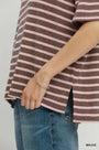 A close-up of a person wearing a brown and pink striped short-sleeve top with blue jeans, showing a thin silver chain bracelet on the wrist. The word 'MAUVE' appears in the bottom right corner.