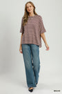 A woman modeling an oversized short-sleeve t-shirt with horizontal mauve and white stripes, paired with wide-leg blue jeans, against a light gray studio background.