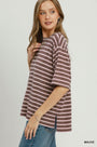 A woman modeling a short-sleeve knit top with horizontal mauve and brown stripes, paired with blue jeans, against a light gray studio background.