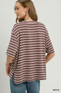 A woman shown from the back wearing an oversized short-sleeve striped top in mauve and off-white, paired with blue jeans, against a plain light gray studio background.