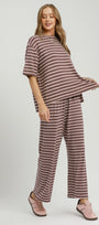 A woman modeling a two-piece loungewear set featuring a short-sleeve top and matching wide-leg pants with horizontal mauve and white stripes, set against a plain light gray studio background.
