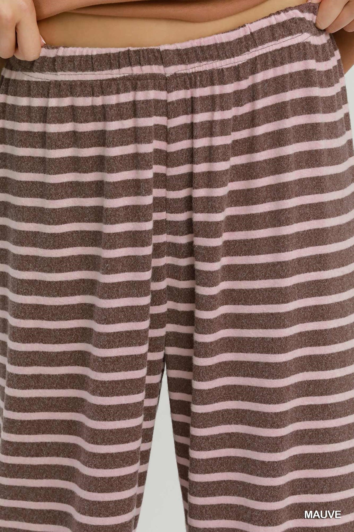 Close-up of a person wearing striped lounge pants in mauve and light pink, with the waistband and hands visible at the top.