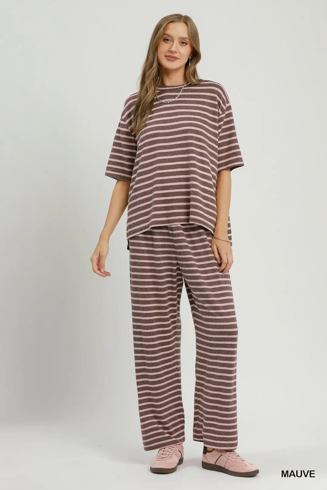 A woman modeling a matching two-piece loungewear set consisting of a short-sleeve crewneck top and wide-leg pants, both in a brown and white horizontal stripe pattern. She is wearing mauve-colored slip-on shoes.