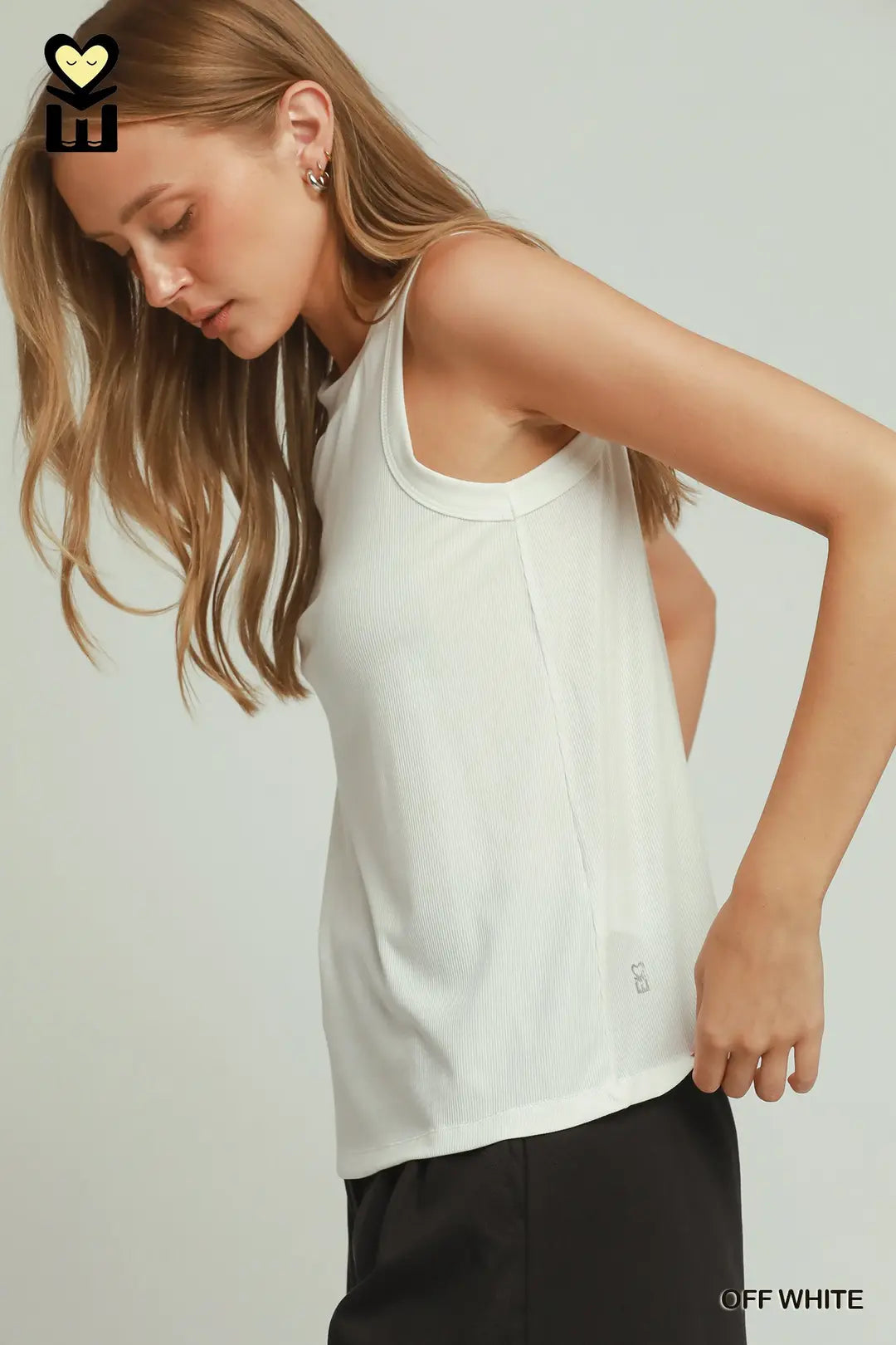 A woman wearing a sleeveless off-white tank top and black pants, photographed against a light gray studio background. The text 'OFF WHITE' appears in the bottom right corner.