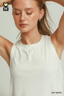 A woman wearing a sleeveless off-white ribbed tank top, shown from the chest up with her arms raised against a light gray studio background. The text 'OFF WHITE' appears in the bottom right corner.