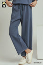A person wearing wide-leg denim blue pants with a drawstring waist, paired with white sneakers, shown from the waist down against a light gray studio background.