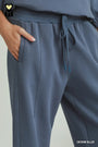 Close-up of a person wearing wide-leg drawstring sweatpants in a dusty denim blue color, with a hand in the pocket and a text label reading 'DENIM BLUE' in the corner.