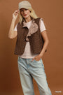 A woman models a brown sleeveless vest with a polka dot pattern and a ruffled collar, styled over a light pink t-shirt and light blue jeans against a solid brown background.