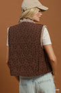 A woman shown from the back wearing a brown quilted vest with a small black polka dot pattern, layered over a white ribbed t-shirt and light blue jeans. She is also wearing a beige baseball cap.
