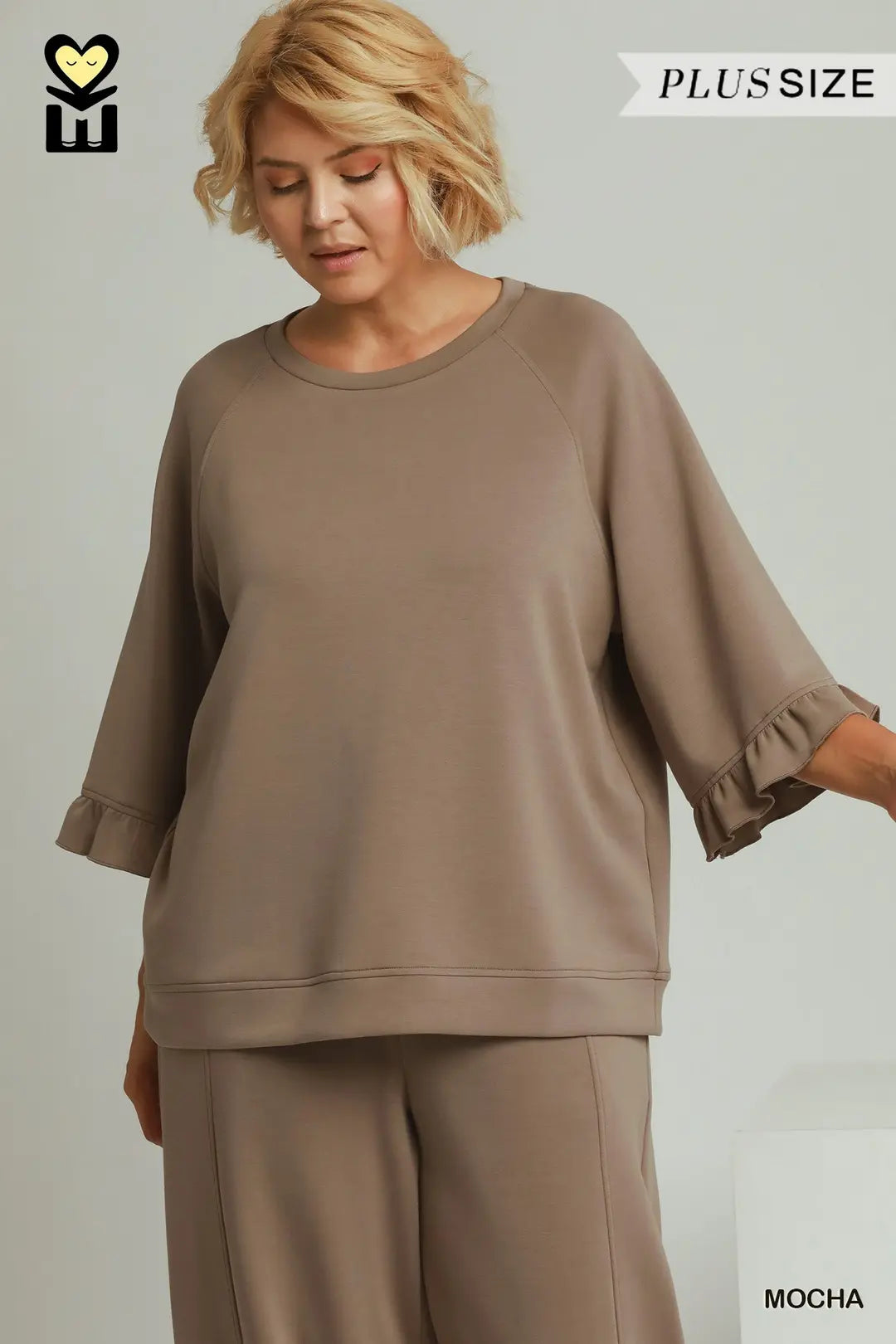 A woman wearing a matching two-piece lounge set in mocha brown, featuring a relaxed-fit sweatshirt with ruffled elbow-length sleeves and matching wide-leg pants. The image includes 'PLUS SIZE' and 'MOCHA' text overlays.