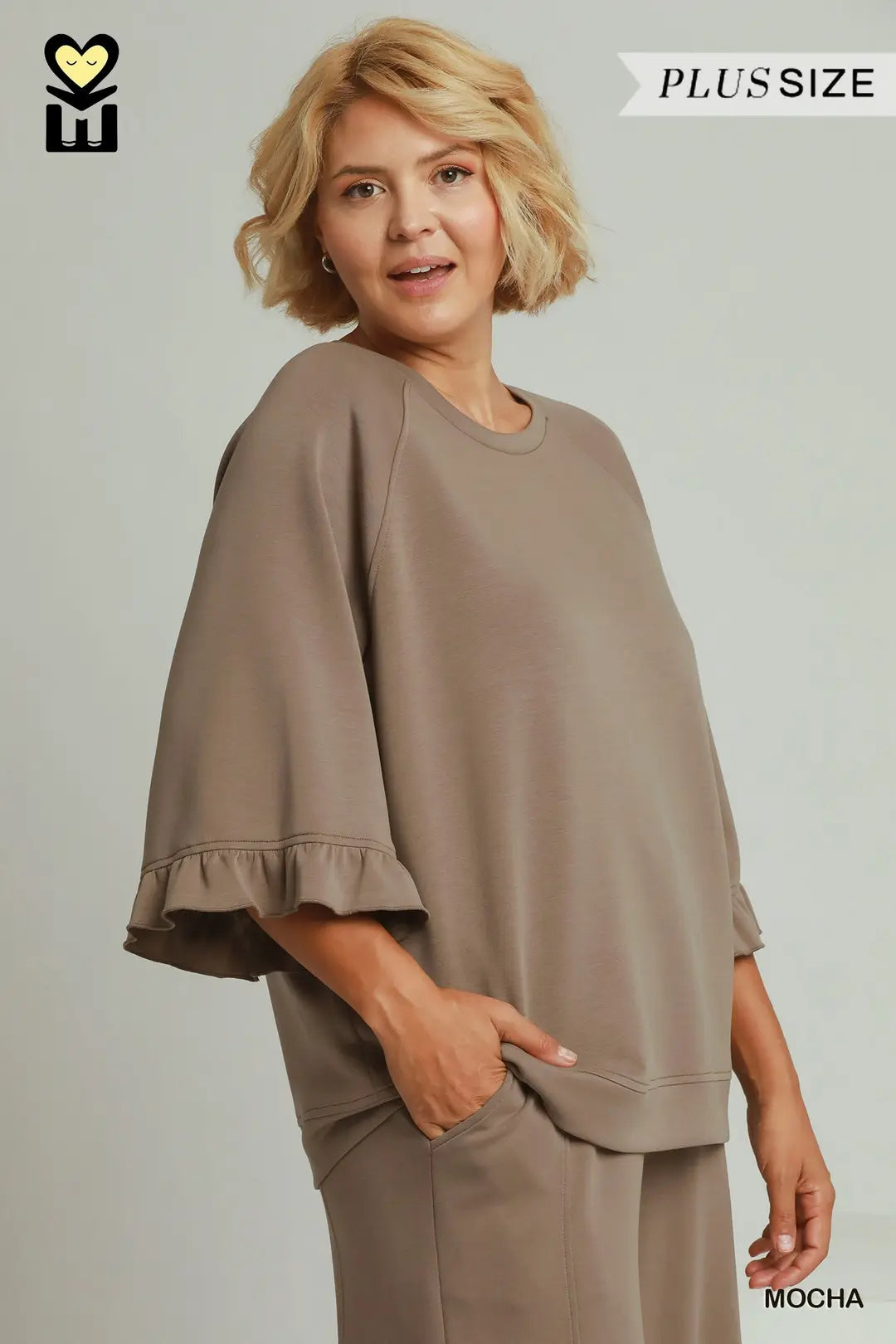 A woman modeling a loose, oversized taupe-brown lounge set with wide flutter sleeves and ruffled cuffs, shown against a plain light gray studio background. Text overlays read PLUSSIZE and MOCHA.