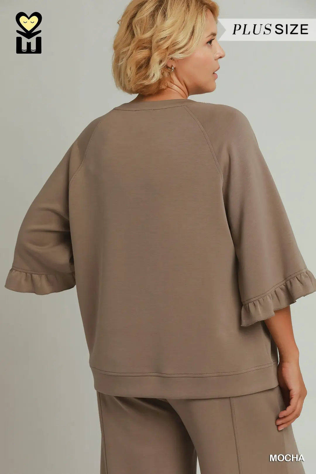 A woman shown from the back wearing a taupe-brown lounge set with wide three-quarter sleeves and ruffled cuffs, photographed against a plain light gray studio background. Text overlays read PLUS SIZE and MOCHA.