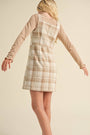 Person wearing a plaid dress over a long-sleeve shirt against a beige background