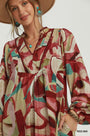 A woman wearing a loose, long-sleeve bohemian-style dress with an abstract watercolor print in red, beige, and teal, paired with a wide-brimmed tan hat and turquoise jewelry. A 'RED MIX' label is visible in the bottom right corner.
