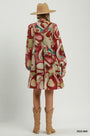 A model shown from the back wearing a tiered long-sleeve dress with an abstract red, beige, and teal pattern, styled with a tan hat and tan cowboy boots against a light gray studio background.