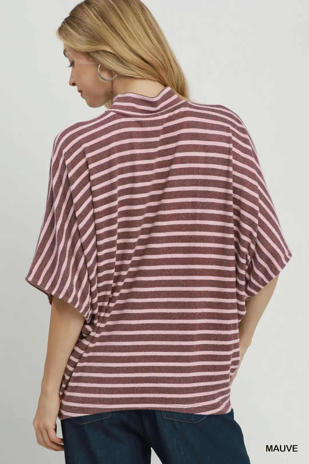 A woman shown from the back wearing a loose, short-sleeve striped top in mauve and white, paired with dark blue jeans, against a plain light gray studio background.