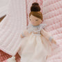 Plush doll with a white dress and brown hair on a pink textured background