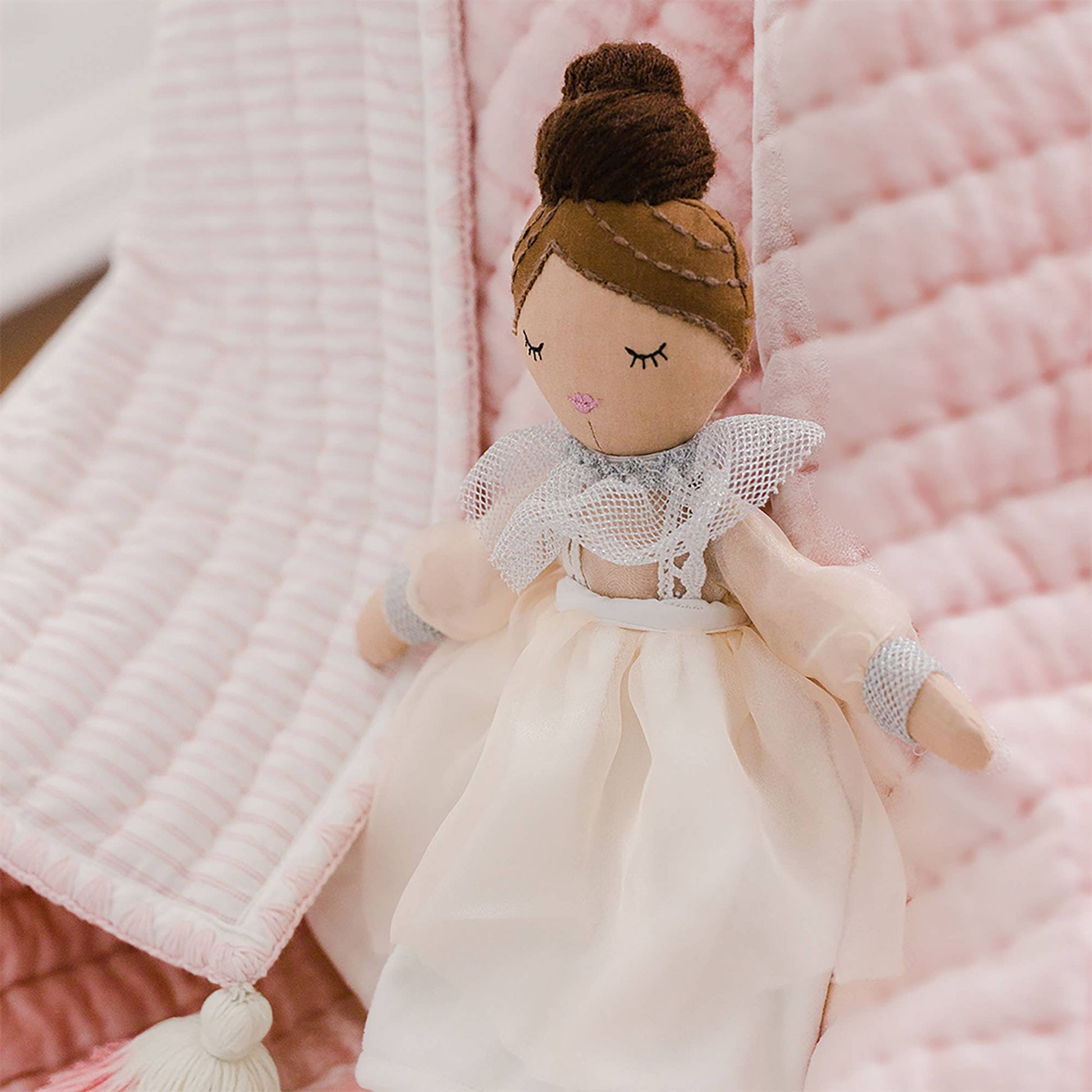 Plush doll with a white dress and brown hair on a pink textured background