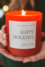 Red candle labeled 'Happy Holidays' held by a hand with blurred lights in the background