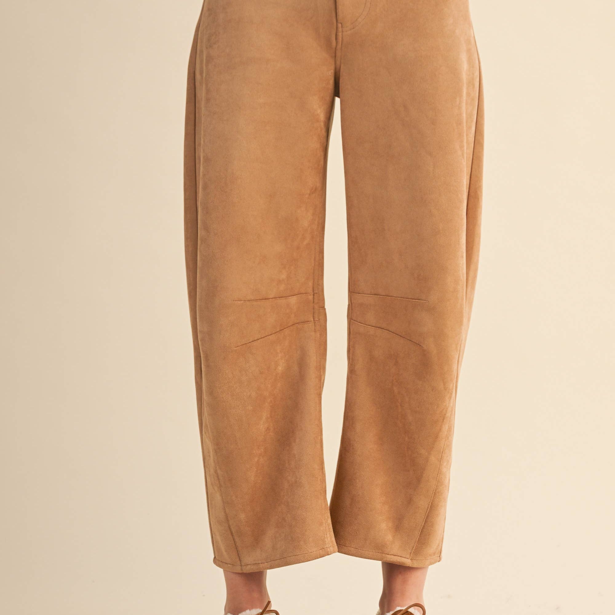 Tan suede pants worn by a person on a beige background