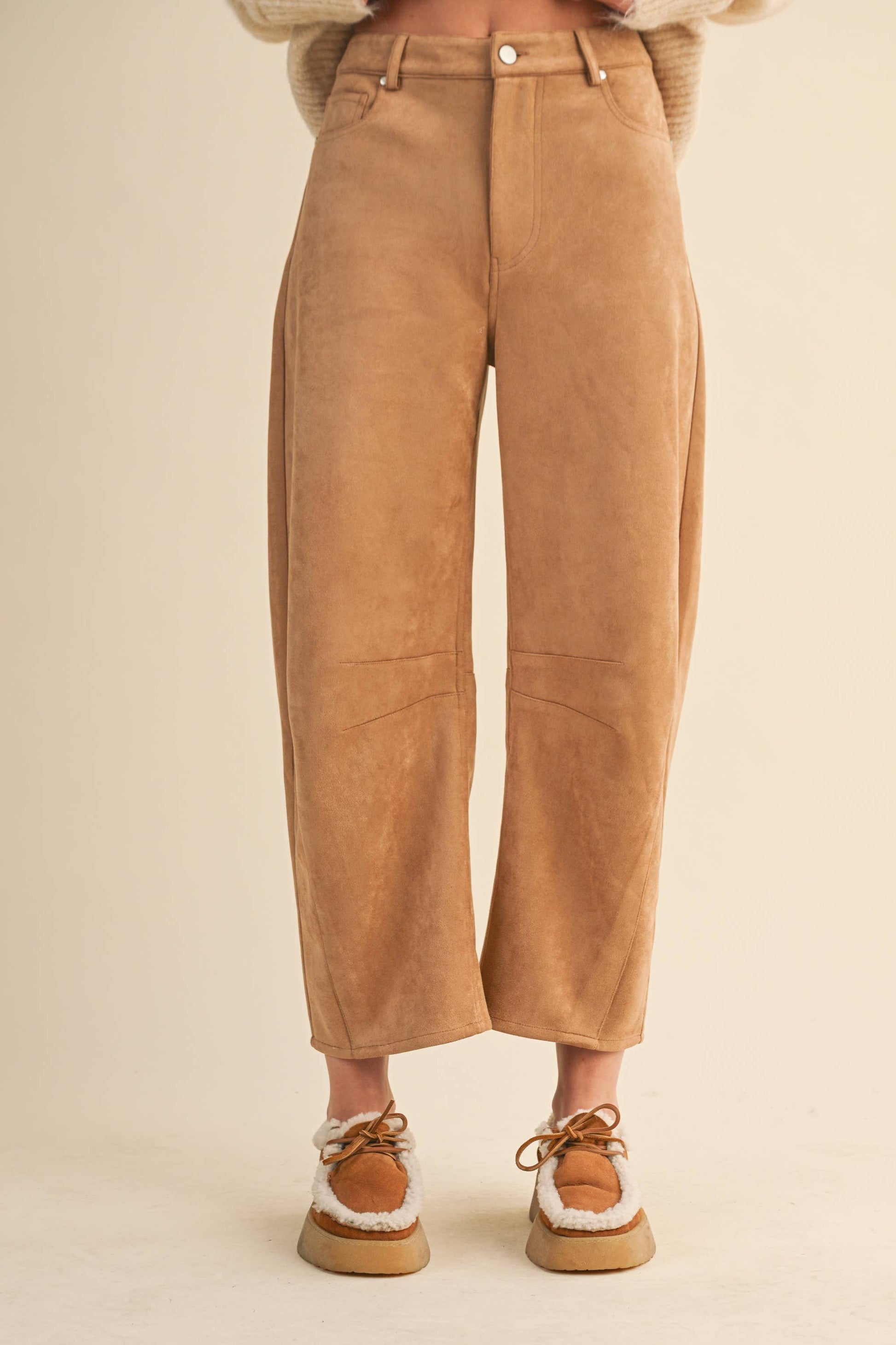 Tan suede pants worn by a person on a beige background