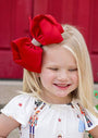 Child wearing a large red bow headband with a red curtain background