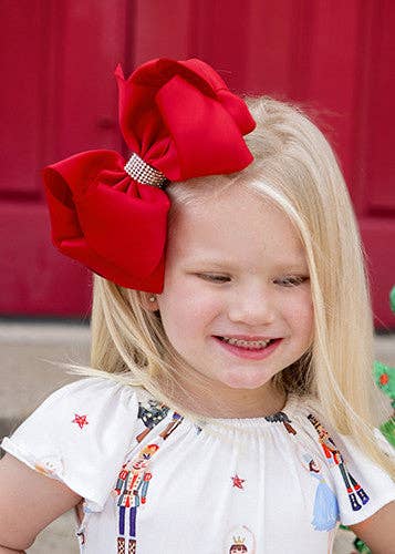 Child wearing a large red bow headband with a red curtain background