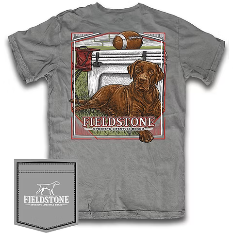 A gray short-sleeve graphic t-shirt featuring a large front print of a brown dog, a football, and the text 'FIELDSTONE'. A matching gray fabric pocket patch with the Fieldstone logo is shown in the bottom-left corner against a white background.