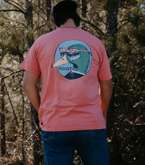 Person wearing a pink t-shirt with a graphic design in a forest setting