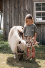 Young girl interacting with a small pony in front of a wooden building.