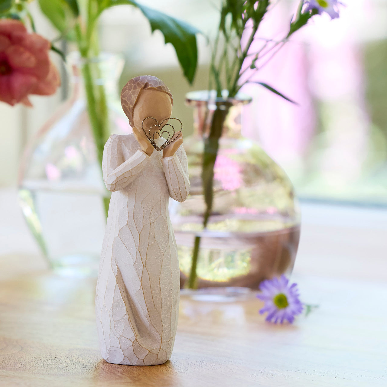 Decorative figurine of a woman holding a heart-shaped object on a blurred floral background