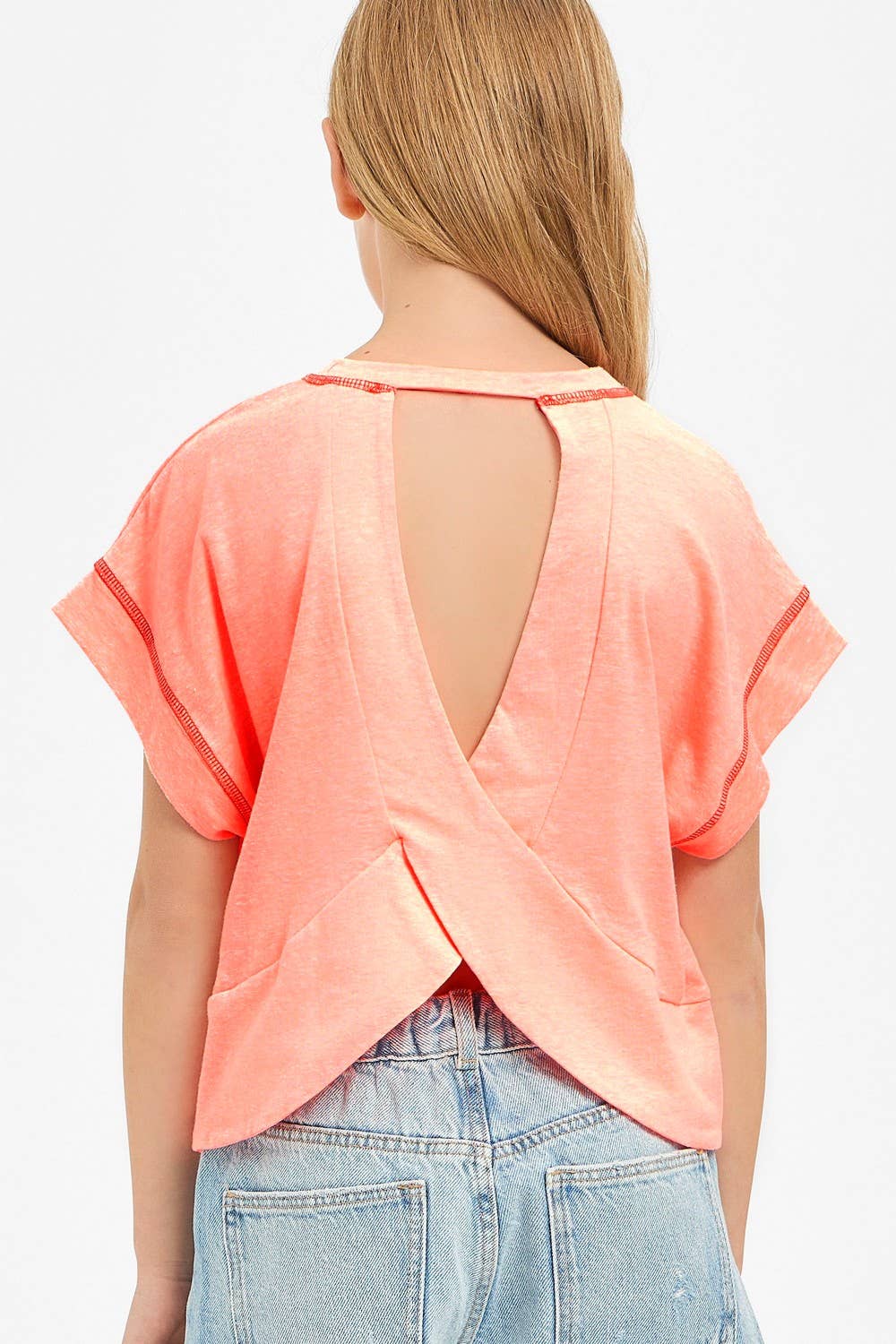 Woman wearing a peach-colored open-back top with denim shorts on a white background