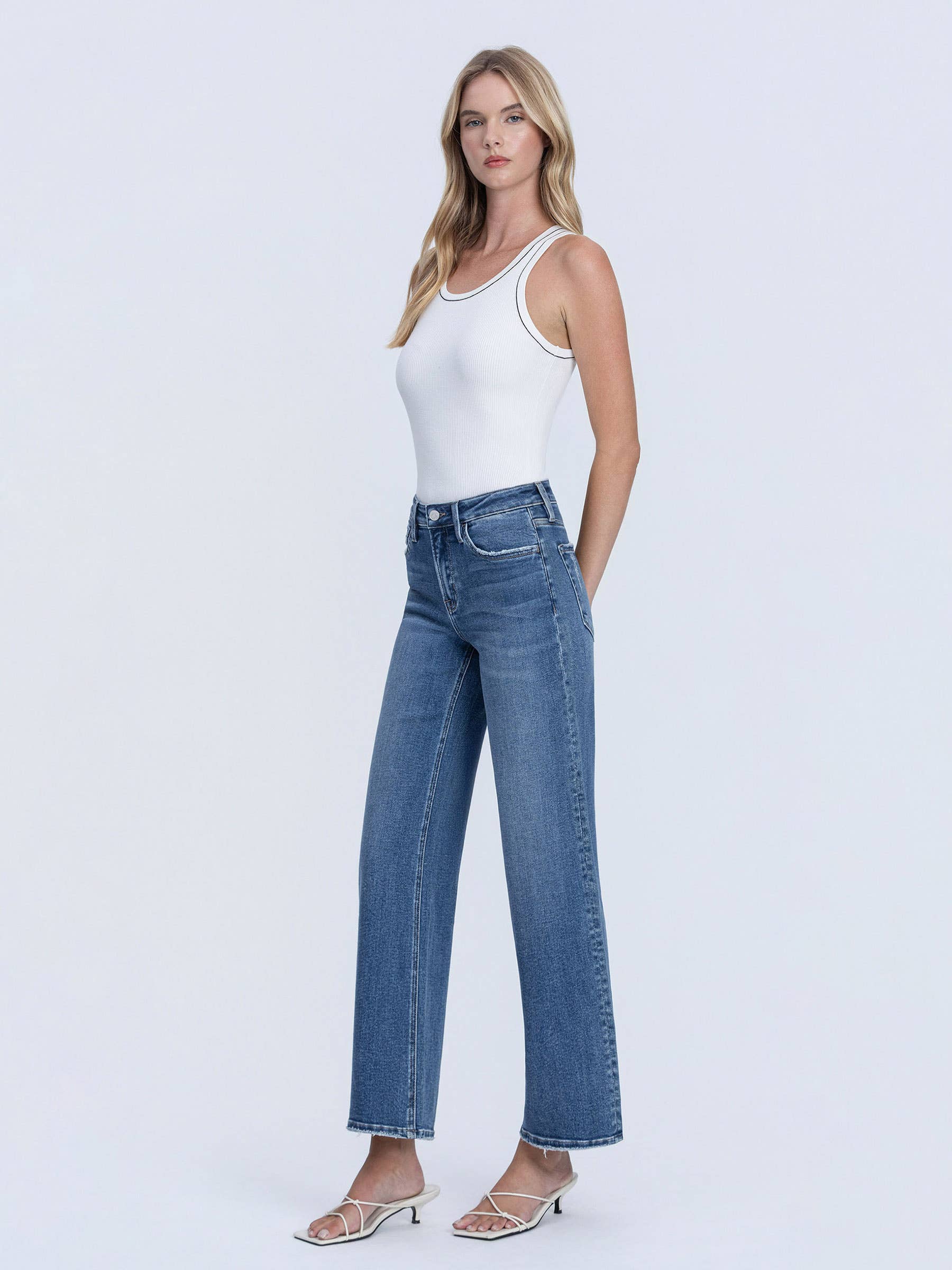 Woman wearing a white tank top and blue jeans on a white background