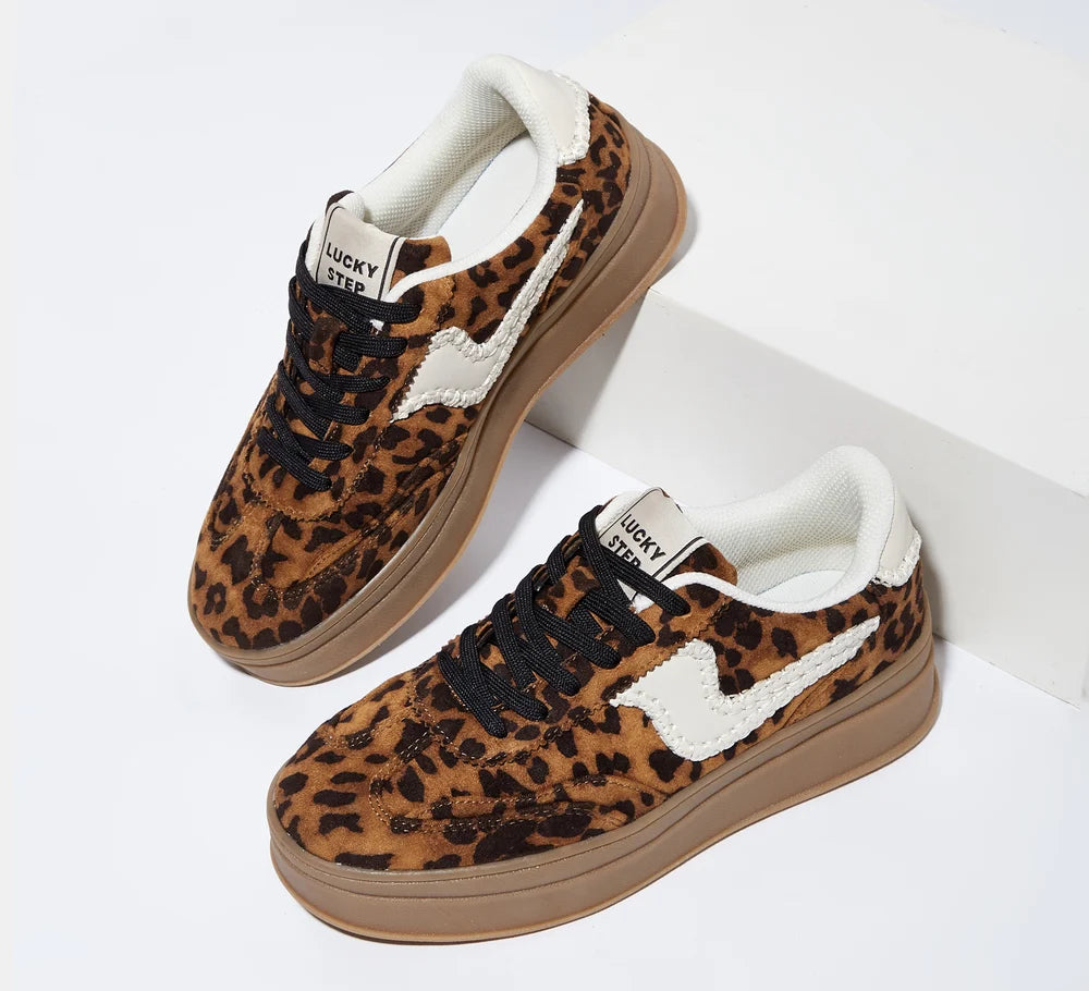 A pair of low-top sneakers with a brown and black leopard print upper, white side accents, black laces, and a gum sole, displayed on a clean white background.