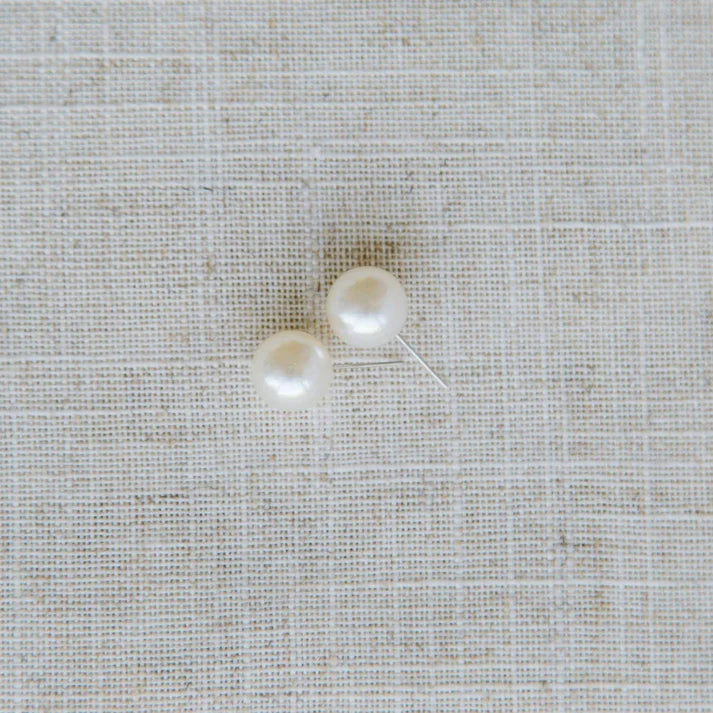 Two pearl earrings on a textured beige fabric background