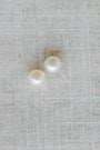 Two pearl earrings on a textured beige fabric background