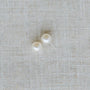 Two pearl earrings on a textured beige fabric background