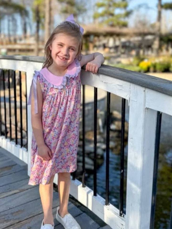Young girl in a floral dress standing on a wooden deck with a scenic background.