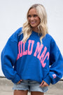 Woman wearing a blue sweatshirt with pink text, standing against a plain background