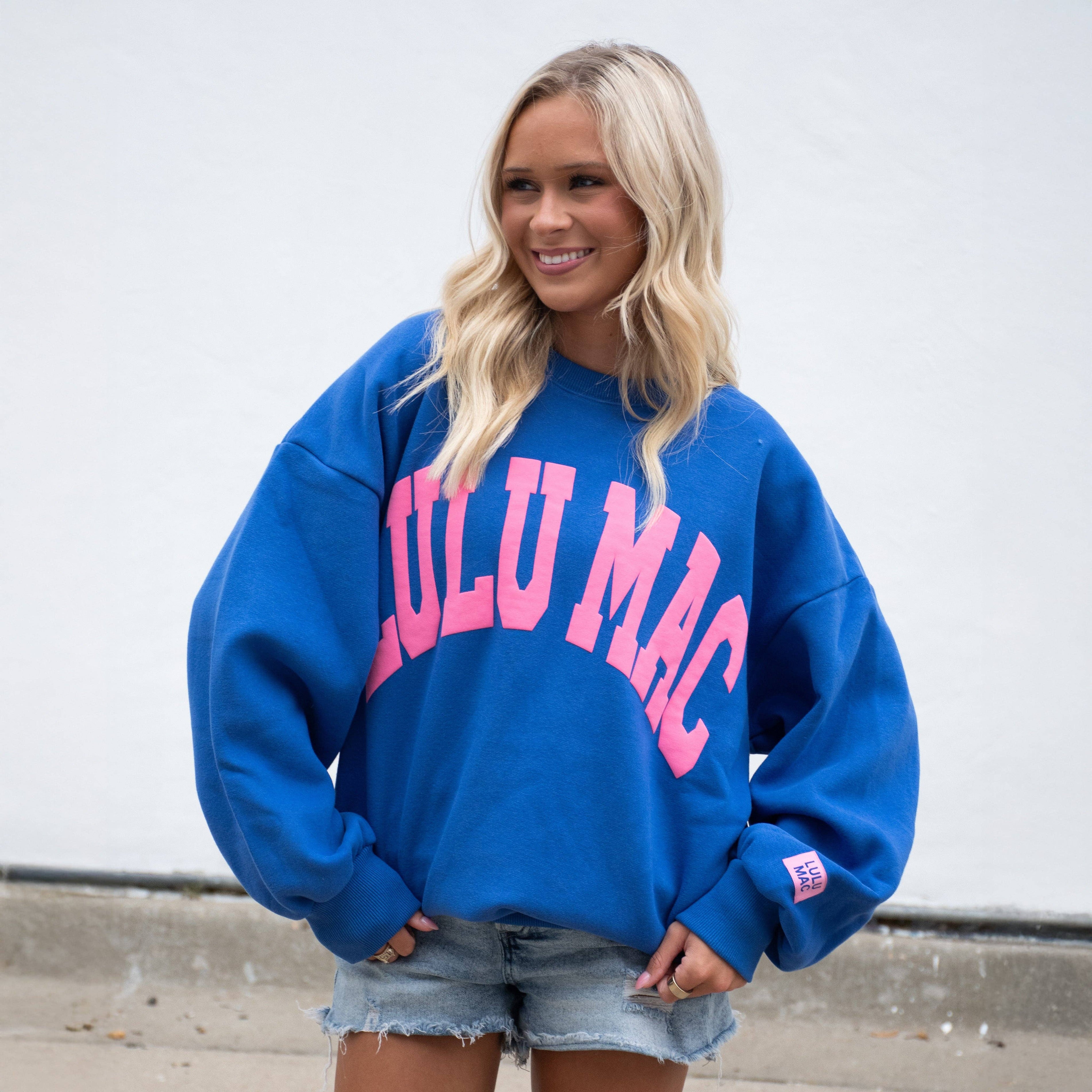 Woman wearing a blue sweatshirt with pink text, standing against a plain background