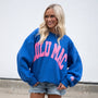 Woman wearing a blue sweatshirt with pink text, standing against a plain background